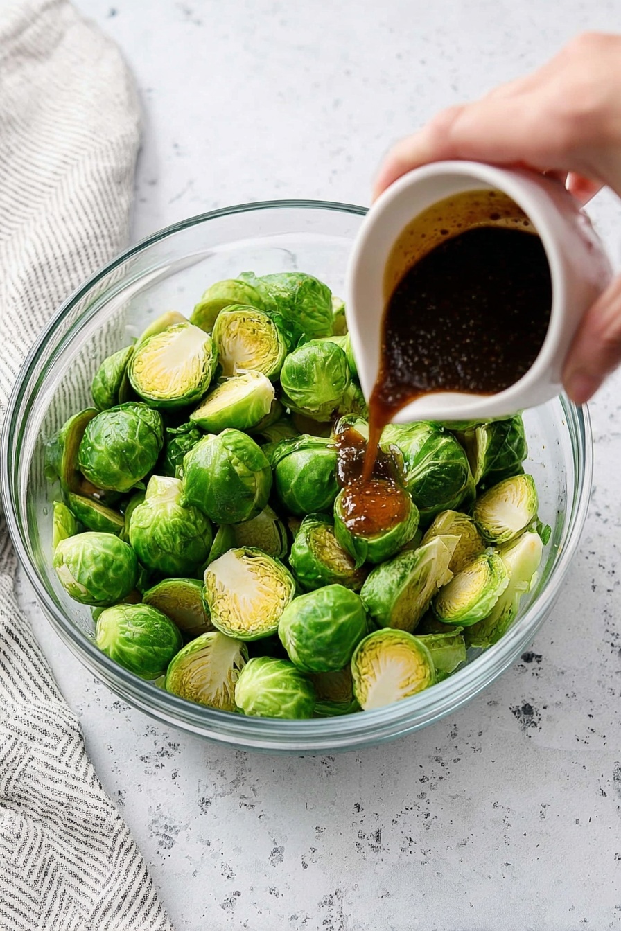 A clear glass bowl filled with green Brussels sprouts that are cut in half, showing the light green inner layers with a firm texture. A woman's hand is holding a small white cup pouring a dark, thick sauce onto the Brussels sprouts. The surface beneath is a white marbled texture, and there is a white and grey striped cloth on the left side. The lighting is bright and natural, highlighting the fresh green color of the sprouts and the deep brown color of the sauce photo taken with an iphone --ar 2:3 --v 7